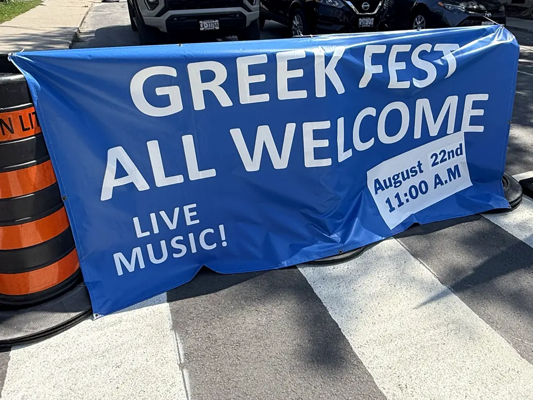 A blue Greek Fest “All welcome” banner on a downtown Kingston street